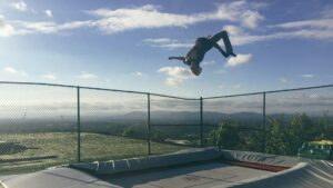 Person springt auf einem Trampolin vor Bergpanorama im Freizeitpark